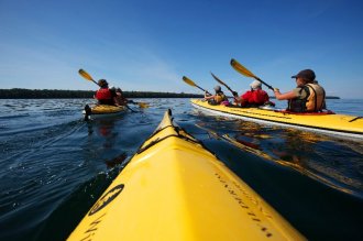 Adults paddling three yellow kayaks on Lake Superior.