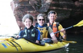 Parents and daughter explore the Mawikwe Bay sea caves in a yellow kayak.