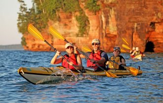 Three kayakers in a yellow kayak paddle on the lake with red sandstone cliffs in the background.