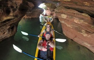 Three people in a yellow kayak paddling through a sea cave.